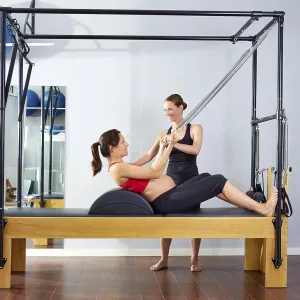 Pregnant woman pilates reformer roll up cadillac exercise with personal trainer Pregnant woman pilates reformer roll up cadillac exercise with personal trainer