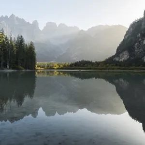 A quiet lake (Toblach lake) reflects the surrounding mountains in the soft evening light