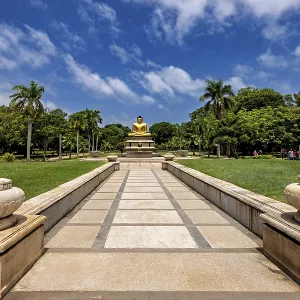 Quiet park with centrally placed Buddha statue and stone path under blue sky Quiet park with centrally placed Buddha statue and stone path under blue sky