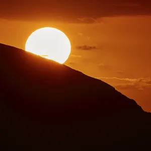 Radiant sun over a mountain in an intense orange sky at sunset Radiant sun over a mountain in an intense orange sky at sunset