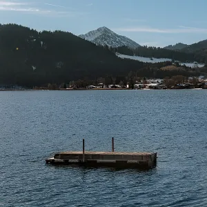 A raft on the lake in front of snow-covered Alps surrounded by dark hills under a blue sky