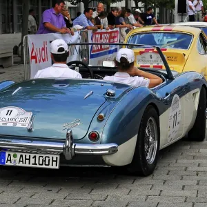 Rear view of a blue convertible and a yellow Porsche during a classic car rally in the city