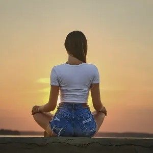 Rear view of a woman in meditation pose on the pier during summer sunset