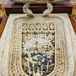 A reclining Buddha statue with gold robes above a carved stone surface filled with coins A reclining Buddha statue with gold robes above a carved stone surface filled with coins