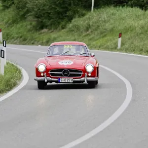 A red classic Mercedes-Benz drives on a winding country road during a classic car race A red classic Mercedes-Benz drives on a winding country road during a classic car race