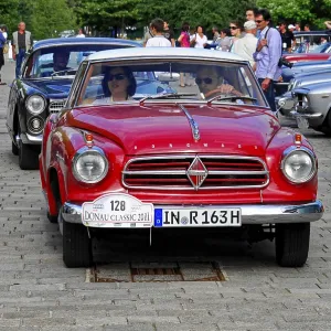 Red coupe vehicle at a vintage car event surrounded by people and other cars