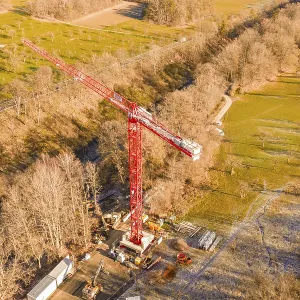 Red crane on construction site in autumn landscape with forests and meadows from a bird's eye view Red crane on construction site in autumn landscape with forests and meadows from a bird's eye view