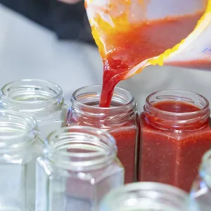 Red liquid is poured from a measuring cup into empty jars Red liquid is poured from a measuring cup into empty jars