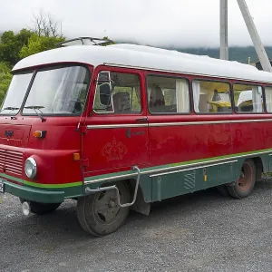 Red retro bus with green stripes on a road in a rural mountain landscape