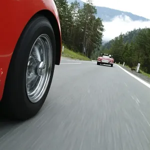 Red TR 3 driving behind a red vintage car