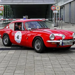A red Triumph classic car drives on a road
