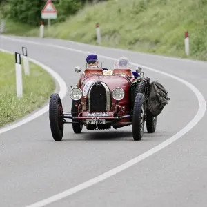 A red, vintage racing car drives along a winding country road A red, vintage racing car drives along a winding country road