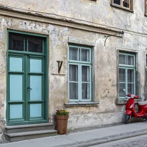 A red vintage scooter on a pedestrian sidewalk in front of an old stone house