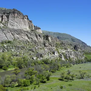 A river flows through a green valley with rocky slopes and trees