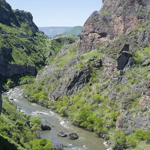 A river flows through a narrow green gorge with steep rocky slopes