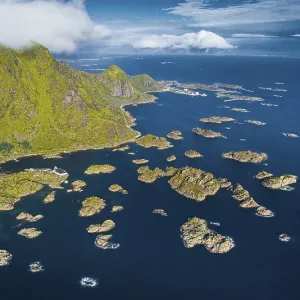 Road to Henningsvaer, numerous small rocky islands in the sea in front of green Lofotenberg