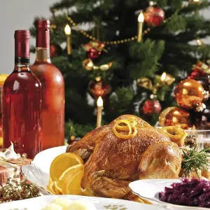 Roast turkey on a festive table setting served with red cabbage and dumplings in front of a decorated Christmas tree