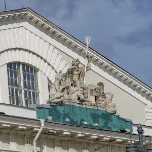 Roof of a historic building with Poseidon sculptures against a cloudy sky
