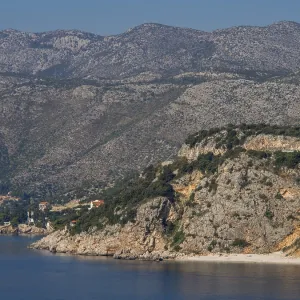 Rough coastline with large rocks and massive mountains behind them on the clear sea Rough coastline with large rocks and massive mountains behind them on the clear sea