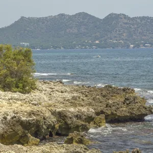Rough rocks border the sea with mountains in the background along the coast