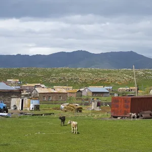 Rural settlement with huts and animals on a green pasture surrounded by mountains under a cloudy sky Rural settlement with huts and animals on a green pasture surrounded by mountains under a cloudy sky