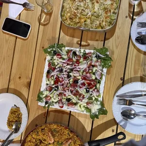 Rustic wooden table set with multiple homemade dishes including a large pan of seafood paella