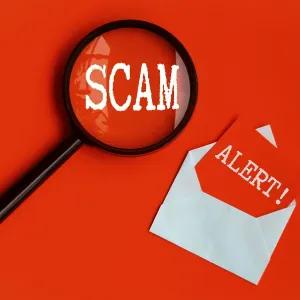 Scam Alert text on magnifying glass and notepad on red cover background