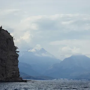 Scenic view of a rocky shoreline with distant mountains under a cloudy sky