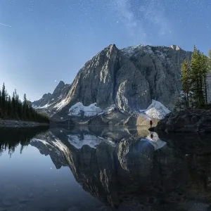 A serene mountain landscape with calm lake reflections under a starry night sky