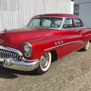 A shiny red classic car with chrome details parked in front of a white garage door