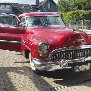 A shiny red vintage car with chrome details parked on a street on a sunny day A shiny red vintage car with chrome details parked on a street on a sunny day