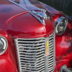 Front of a shiny red vintage car with a striking emblem in the sun