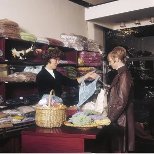Shopping in the 1960s. Interior of a fashion shop where a woman is showing a female customer a swimming costume