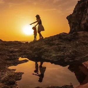 Silhouette of mother and son walking in the sunset on the beach of Tacoron in El Hierro Silhouette of mother and son walking in the sunset on the beach of Tacoron in El Hierro