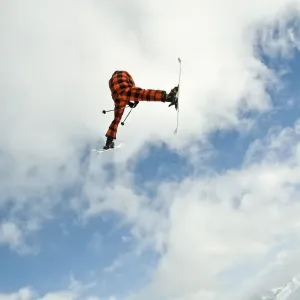Skier jumping in front of a blue sky with a snow-covered mountain range behind