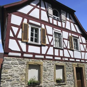 Maison à colombages petite avec des poutres rouges et une fondation en pierre.