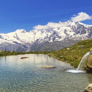 Small waterfall flows into a clear mountain lake against a mountain backdrop
