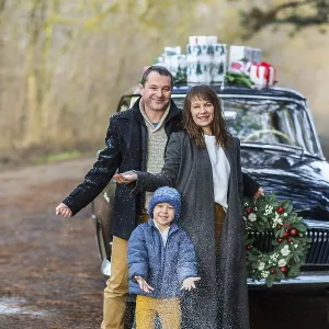 Smiling adult man and woman with boy in warm clothes standing at vintage car with Christmas presents Smiling adult man and woman with boy in warm clothes standing at vintage car with Christmas presents