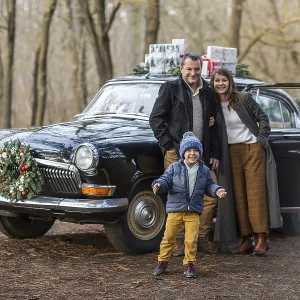 Smiling adult man and woman with boy in warm clothes standing at vintage car with Christmas presents Smiling adult man and woman with boy in warm clothes standing at vintage car with Christmas presents