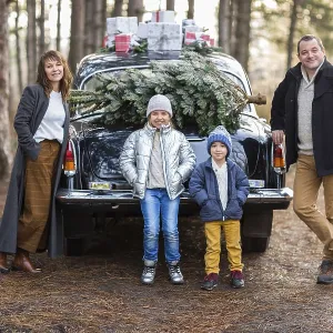 Smiling adult man and woman with kids in warm clothes standing at vintage car with Christmas presents Smiling adult man and woman with kids in warm clothes standing at vintage car with Christmas presents