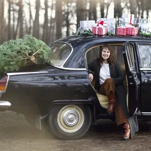 Smiling adult woman in warm clothes by vintage car with Christmas presents Smiling adult woman in warm clothes by vintage car with Christmas presents
