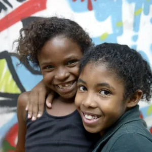 Two smiling girls embracing each other in front of a graffiti-sprayed wall Two smiling girls embracing each other in front of a graffiti-sprayed wall