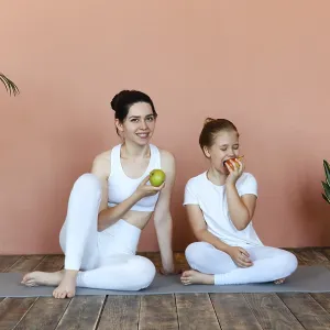 Smiling woman and little girl eating fruits after practicing yoga on mat in cozy living room Smiling woman and little girl eating fruits after practicing yoga on mat in cozy living room