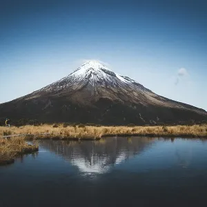 A snow-capped mountain is reflected in a still lake while people walk along the shore A snow-capped mountain is reflected in a still lake while people walk along the shore