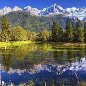 The snow-covered Alps and evergreen fir-trees are reflected in lake