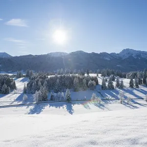 Snow-covered landscape with bright sun over mountains and trees Snow-covered landscape with bright sun over mountains and trees