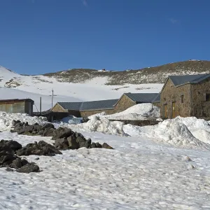 Snow-covered landscape with stone and metal buildings under a clear blue sky