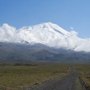 A snow-covered mountain under blue sky with a path in the foreground