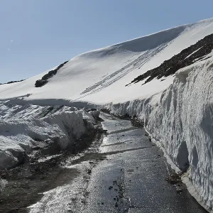 Snow-covered road between snow-covered mountains under a clear blue sky