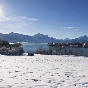 Snowy field with a view of a quiet lake and mountains under a bright sun